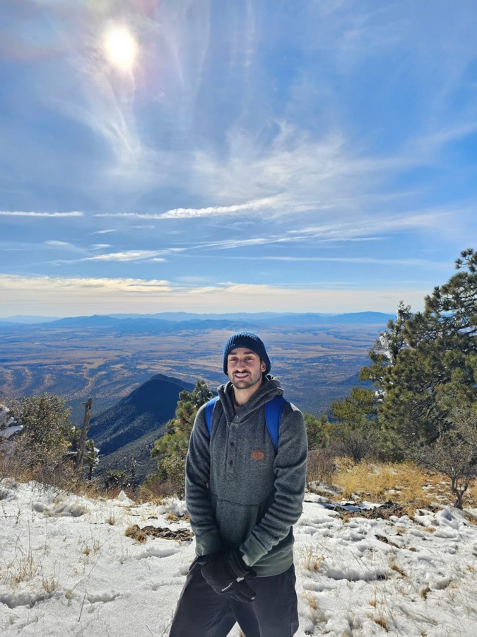 Amir on a snowy mountain summit above a wide valley
